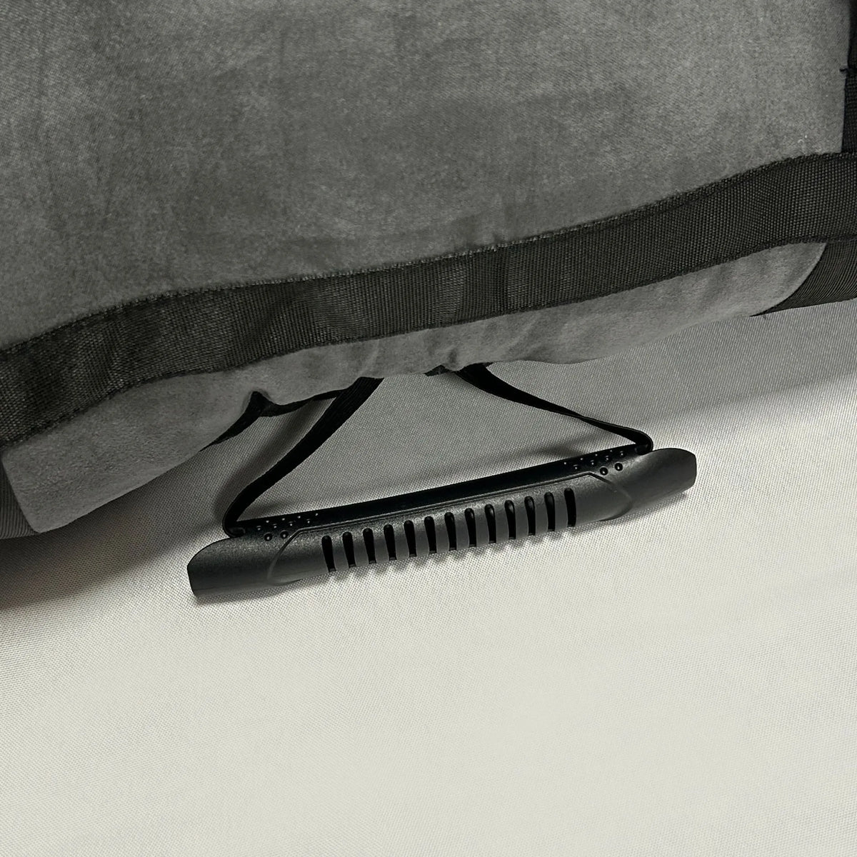 Close-up of a gray fabric item with a black strap and textured black handle resting on a white surface.