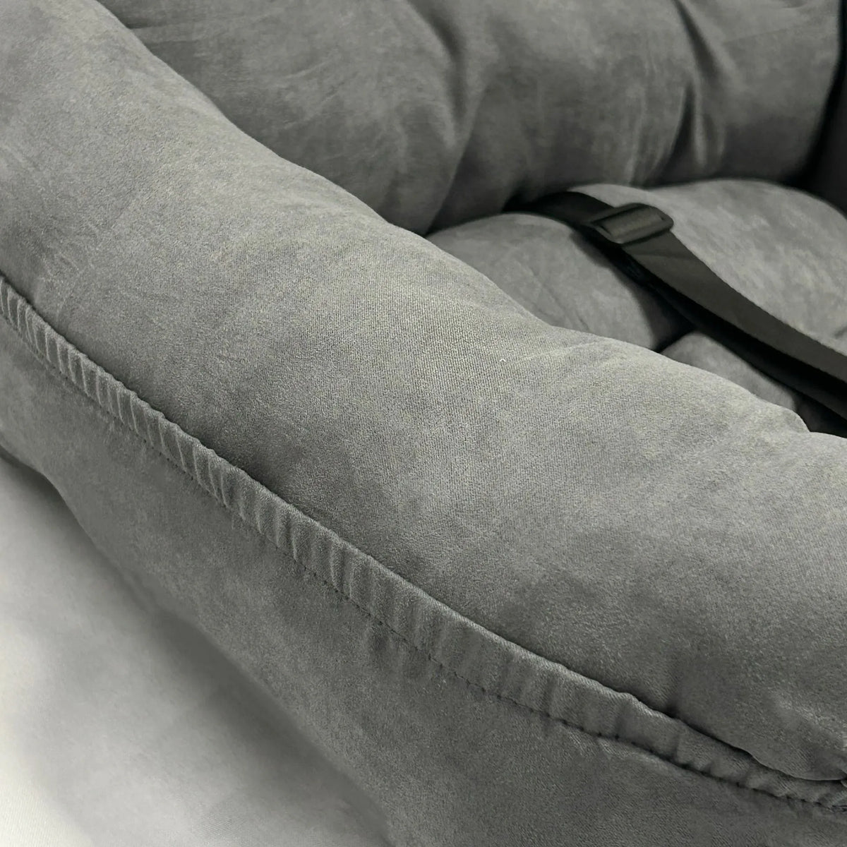 Close-up of a gray plush cushion or pet bed with a black strap, showing the fabric texture and stitching detail.