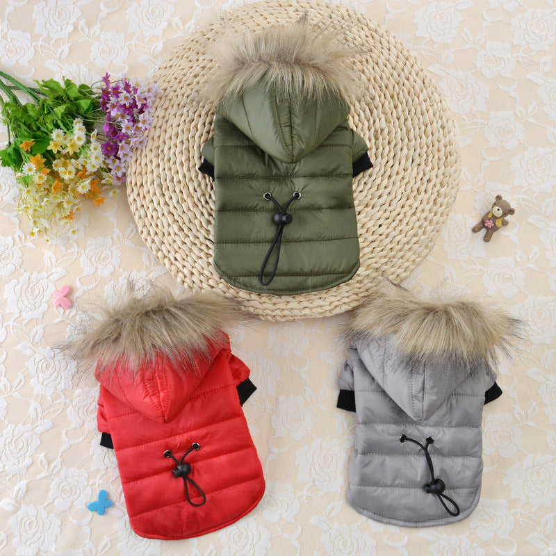 Three dog coats in green, red, and gray with fur-lined hoods on a textured surface.