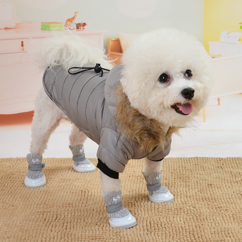 Small dog wearing a gray puffer coat and white boots on a carpeted floor.