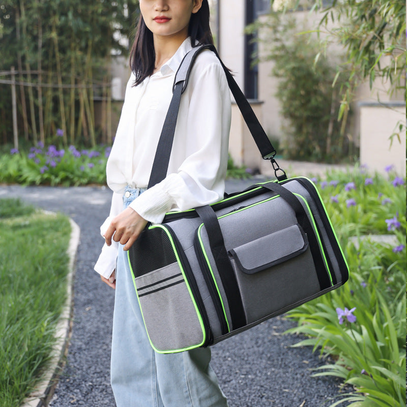 A woman outdoors carrying a gray pet carrier bag with black straps and bright green piping. The bag has a front pocket and side pockets, and the woman is wearing a white blouse and light blue jeans.